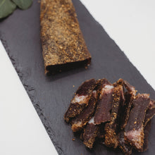 A biltong slab part-sliced on a dark slate board